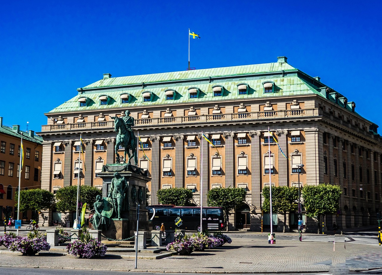 Large several story tall building with lots of windows and a green roof with a tall statue in the front of the building